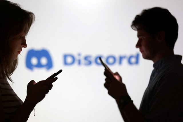 若者たちがスマートフォンを手に持ち、Discordのロゴの前でポーズをとる姿が2025年9月11日に撮影されたイラストです。REUTERS/Dado Ruvic/Illustration