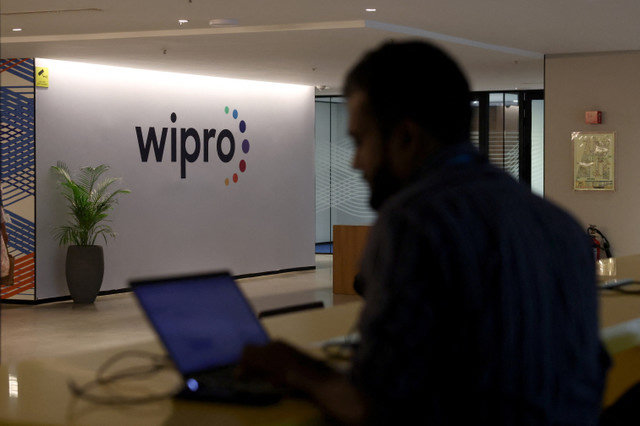 พนักงานคนหนึ่งกำลังทำงานบนแล็ปท็อปของเขาใกล้กับโลโก้ของ Wipro ภายในบริเวณบริษัทในเมืองเบงกาลูรู ประเทศอินเดีย เมื่อวันที่ 13 สิงหาคม 2025 REUTERS/Priyanshu Singh