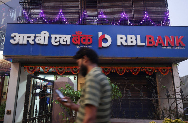 A man uses his phone as he walks past a branch of RBL Bank in Mumbai, India, October 20, 2025. REUTERS/Francis Mascarenhas