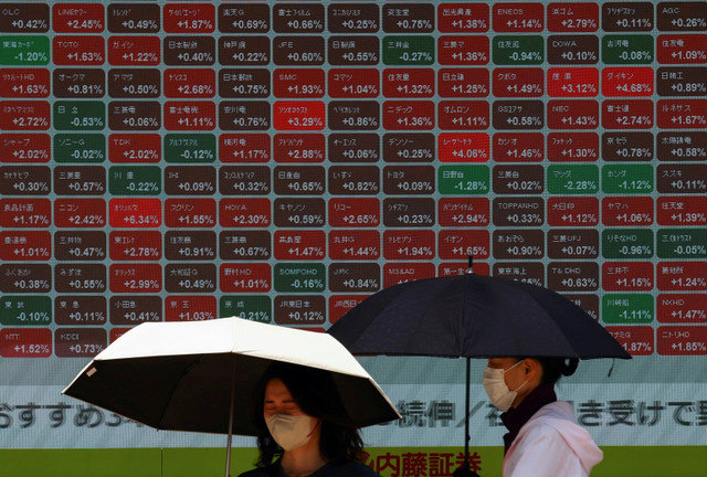 Varias mujeres con paraguas permanecen frente a un tablero de cotizaciones bursátiles frente a una correduría en Tokio, Japón, el 30 de junio de 2025. REUTERS/Issei Kato