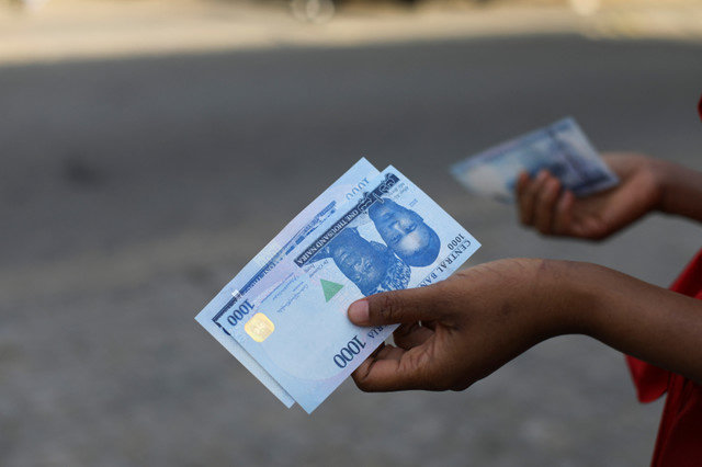 บุคคลหนึ่งถือธนบัตร 1,000 ไนราแบบใหม่ ขณะที่ธนาคารกลางแห่งไนจีเรียเริ่มนำธนบัตรออกใช้สู่สาธารณะผ่านธนาคารต่างๆ ในกรุงอาบูจา ประเทศไนจีเรีย เมื่อวันที่ 15 ธันวาคม 2022 REUTERS/Afolabi Sotunde