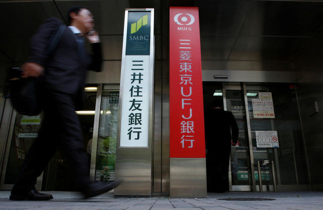 FOTO DE ARCHIVO: Un hombre camina frente a las cabinas de cajeros automáticos de los megabancos de Japón, Sumitomo Mitsui Banking Corporation (izq.) y Bank of Tokyo-Mitsubishi UFJ, en Tokio el 15 de mayo de 2013. REUTERS/Issei Kato/File Photo