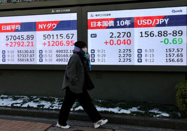 2026年2月9日,在日本东京的一家经纪公司外,一名女子走过显示日经指数、道琼斯工业平均指数、日本10年期国债水平以及美元兑日元汇率的电子屏幕。REUTERS/Kim Kyung-Hoon