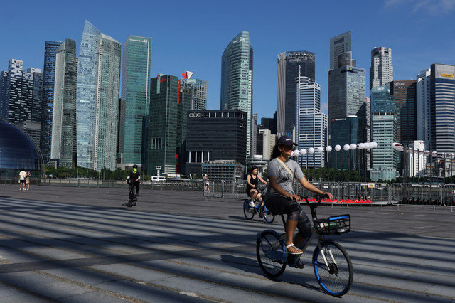 Personas montan en bicicleta frente al horizonte del distrito central de negocios en Singapur el 13 de junio de 2025. REUTERS/Edgar Su/File Photo