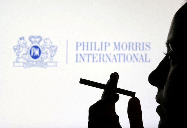 A woman poses with a cigarette in front of the Philip Morris International logo in an illustration taken on July 26, 2022. REUTERS/Dado Ruvic/Illustration/File Photo