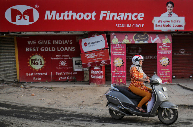 ผู้หญิงขี่สกู๊ตเตอร์ผ่านสาขาของ Muthoot Finance ในเมืองอัห์มดาบาด ประเทศอินเดีย เมื่อวันที่ 21 สิงหาคม 2019 REUTERS/Amit Dave