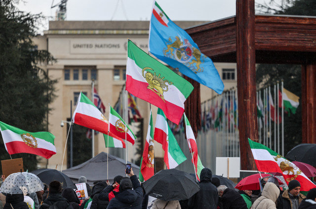 2026年2月17日、スイスのジュネーブで米国とイランによる第2回核協議が行われる中、国連事務局付近に集まった人々がイラン革命前の「獅子と太陽」の国旗を振っている。REUTERS/Pierre Albouy