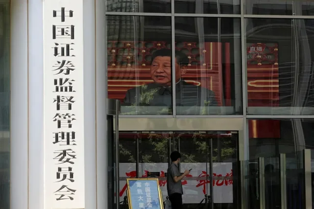 2021年7月9日、中国・北京の金融街にある中国証券監督管理委員会(CSRC)のビルで、習近平国家主席のニュース映像が流れるスクリーンの近くに立つ男性。