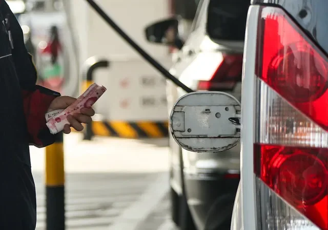 Un empleado sostiene billetes de yuanes chinos junto a la tapa abierta del tanque de combustible de un automóvil en una gasolinera en Pekín, China, ante el anuncio de un aumento de precios. REUTERS/Maxim Shemetov