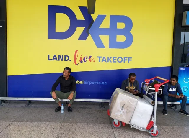 Travelers wait near the official Dubai Airport branding in the Terminal 1 departure area.