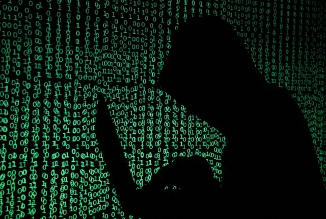 A man in a hood uses a laptop with digital code projected onto him, representing cyber activity. REUTERS/Kacper Pempel/Illustration/File Photo