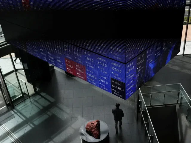 A person walks past a display showing Nikkei stock prices in a Tokyo conference hall, Japan, March 2026. REUTERS/Issei Kato