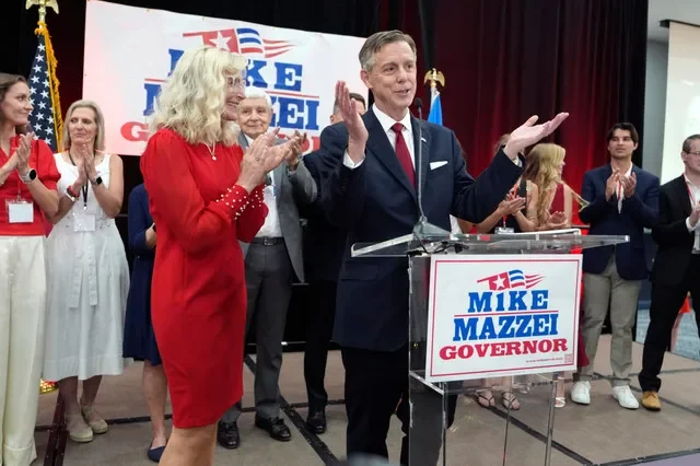 Mike Mazzei stands beside his wife, Noel, as he speaks to supporters in Tulsa, Okla., after winning the GOP runoff election on Tuesday, Aug. 25, 2026.