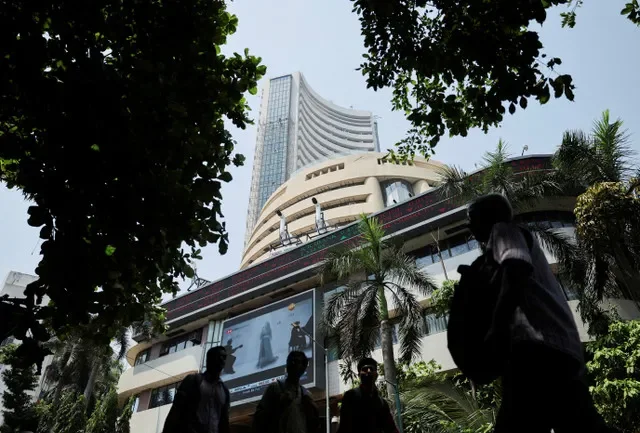 FILE PHOTO: Men walk past a screen displaying market results outside the Bombay Stock Exchange (BSE) in Mumbai, India, April 7, 2025.