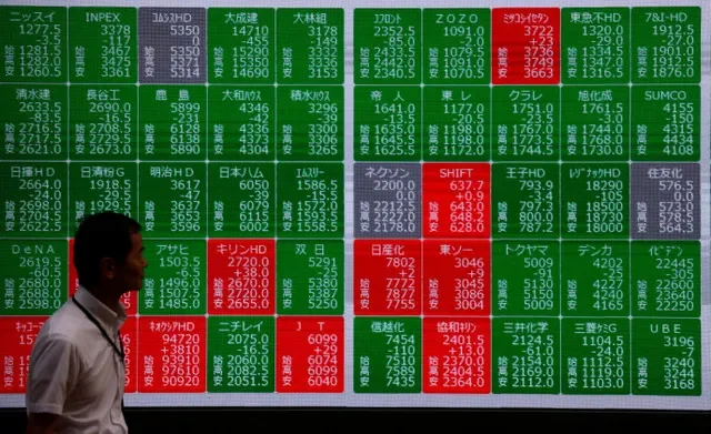 Um homem passa por um painel de cotações de ações que exibe os preços das ações do Nikkei em frente a uma corretora em Tóquio, Japão, em 16 de junho de 2026. REUTERS/Manami Yamada