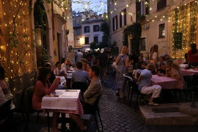 Pessoas jantam ao ar livre em uma rua movimentada no bairro de Trastevere, em Roma, Itália, em 18 de junho de 2026.