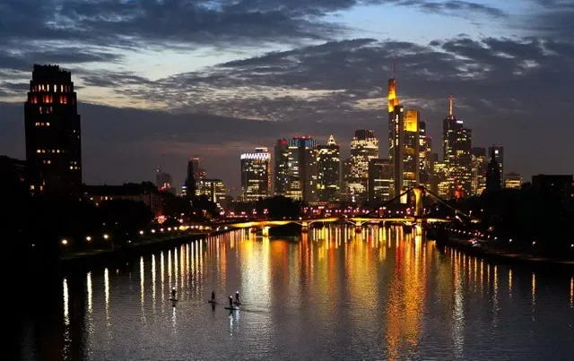 2021年10月18日、ドイツ・フランクフルトの金融街のスカイラインを背景に、夕暮れ時のマイン川でスタンドアップパドルボードを楽しむ人々。 REUTERS/カイ・プファッフェンバッハ