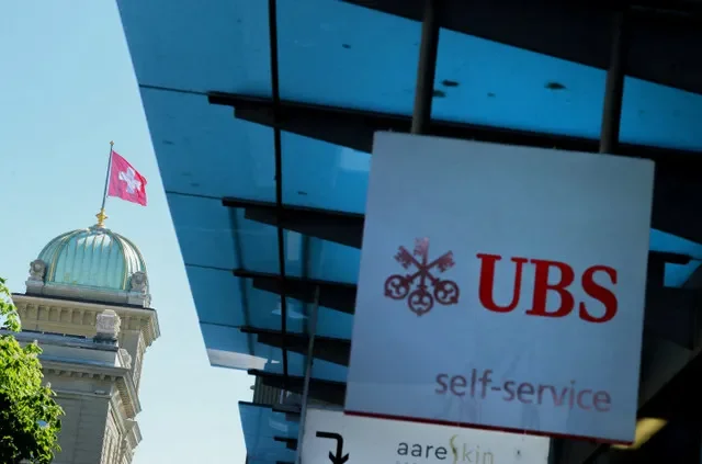 FOTO DE ARCHIVO: Un logotipo de UBS frente a una bandera suiza en el edificio del Parlamento suizo (Bundeshaus) antes de una conferencia de prensa sobre los requisitos de capital de los bancos suizos en Berna, Suiza, el 22 de abril de 2026. REUTERS/Denis Balibouse/Foto de archivo