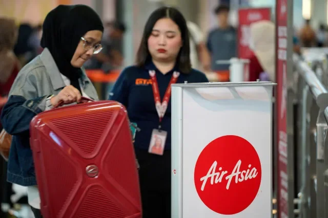 หญิงคนหนึ่งกำลังจัดการสัมภาระข้างโลโก้ AirAsia ที่อาคารผู้โดยสาร 2 ท่าอากาศยานนานาชาติกัวลาลัมเปอร์ (KLIA2) ในเซปัง ประเทศมาเลเซีย วันที่ 18 กันยายน 2026 REUTERS/Najjua Zulkefli