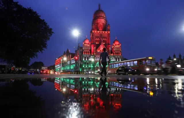 A man walks in front of the Brihanmumbai Municipal Corporation (BMC) building lit up in the colours of India's national flag on the eve of the 75th Independence Day in Mumbai, India, August 14, 2021. REUTERS/Francis Mascarenhas