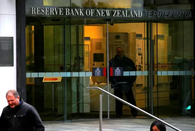 Pedestrians walk past as a security guard stands in the main entrance to the Reserve Bank of New Zealand located in central Wellington, New Zealand, July 3, 2017. REUTERS/David Gray