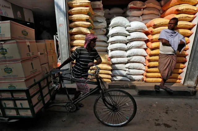 FILE PHOTO: A labourer carries vegetable oil packets on a tricycle as a man stands in front of his shop selling food grains, at a wholesale market in Kolkata, India, January 4, 2017. Picture taken January 4, 2017. REUTERS/Rupak De Chowdhuri/File Photo