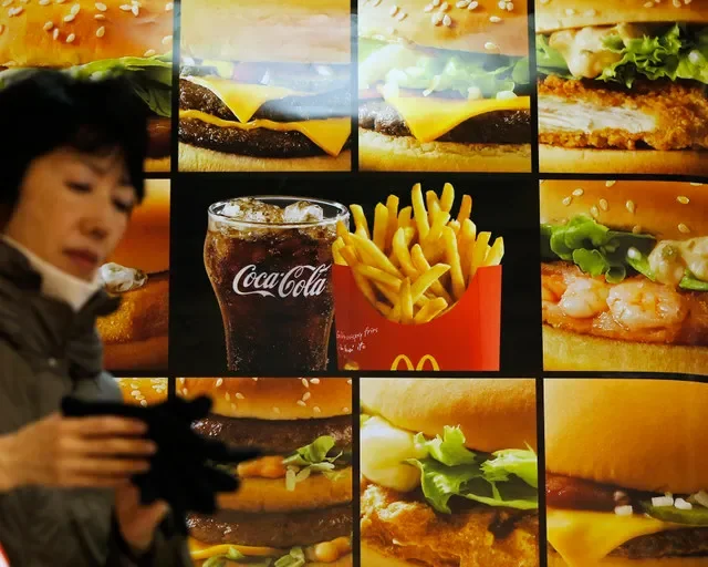 صورة من الأرشيف: امرأة تمر بجانب إعلان يظهر برغر وبطاطس مقلية ومشروباً من McDonald's خارج متجر McDonald's في طوكيو في 16 ديسمبر 2014. REUTERS/إيسي كاتو/صورة من الأرشيف