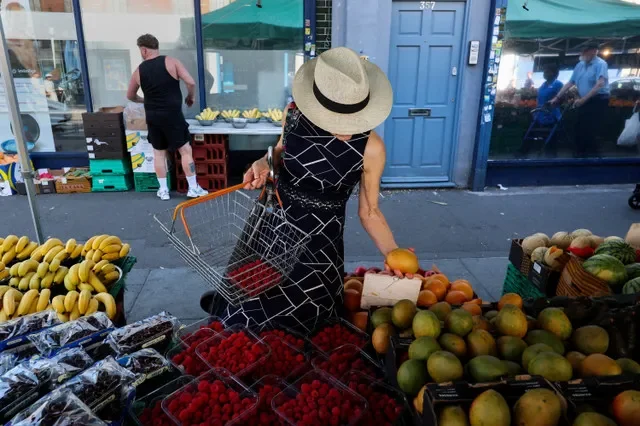 FILE PHOTO: A customer wearing a summer hat chooses produce from a fruit and vegetable stall at North End Road Market in Fulham, London, Britain, June 26, 2026. REUTERS/Kevin Coombs/File Photo