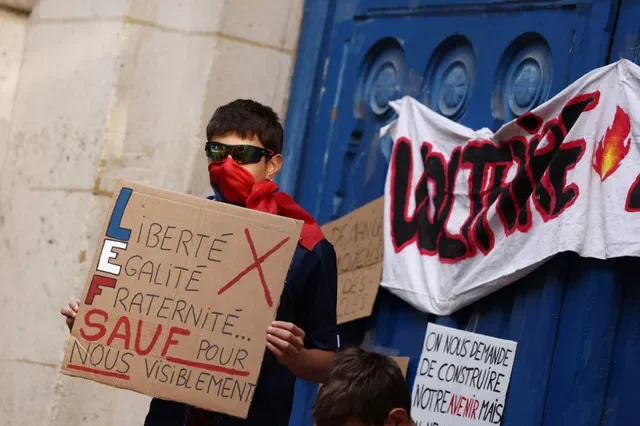 A masked high school student holds a placard reading "Liberty, Equality, Fraternity. Except for us, apparently" during a gathering outside the Lycee Voltaire high school in Paris as part of a nationwide day of demonstrations and blockades, voicing anger over overcrowded classrooms, teacher shortages and dilapidated school buildings, which students blame on years of underinvestment, France, October