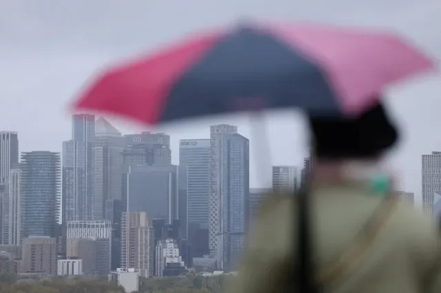 檔案照片:2024年10月28日,英國倫敦,一名女子撐著雨傘,眺望金絲雀碼頭天際線。路透社/霍莉·亞當斯/檔案照片