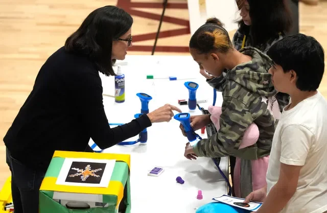 Michele Nelson, de 53 años, consultora de tecnologías emergentes en las Escuelas de Oakland, le explica a Andrea Perryman, alumna de octavo grado de 13 años, el microscopio que observaba durante el Día Nacional de la Nanotecnología en el gimnasio el viernes 9 de octubre de 2026. El distrito escolar de Waterford tiene una propuesta de gravamen operativo en la boleta de noviembre, en lo que representa el segundo intento del distrito por lograr la aprobación de los fondos.