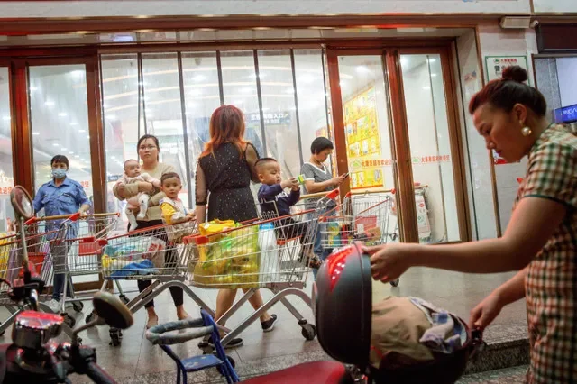 Một phụ nữ bế em bé bên ngoài một siêu thị ở Khâm Châu, khu tự trị Quảng Tây, Trung Quốc, ngày 12 tháng 4 năm 2021. REUTERS/Thomas Peter